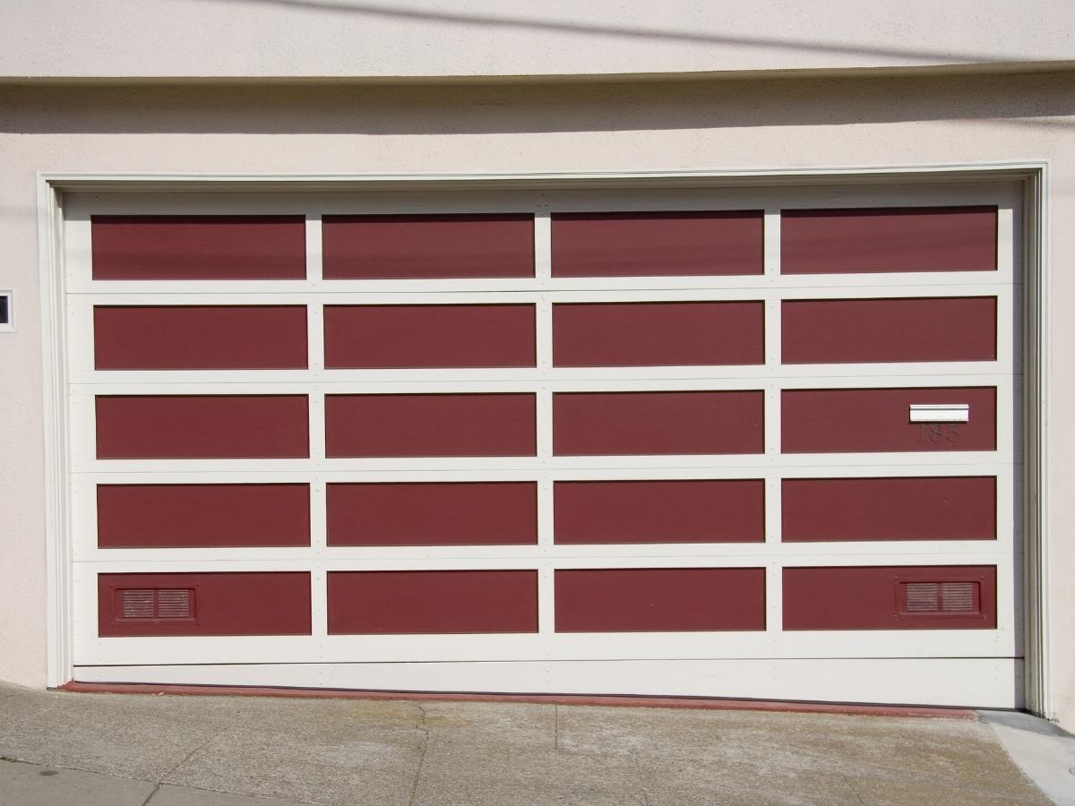 Learn the latest garage door trends for 2023. From colors to windows, trim to style. A red garage door with white panel outlines.
