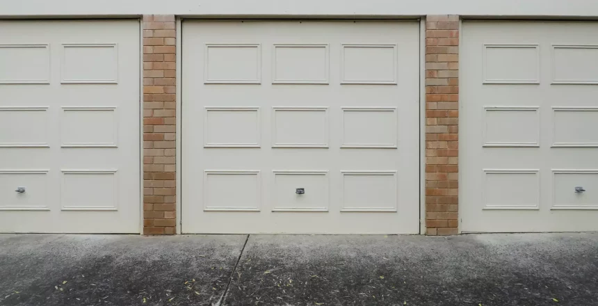 A picture of 3 cream garage doors with wood panels on blonde brick with one of the most most common garage door problems, being stuck closed or very slow.