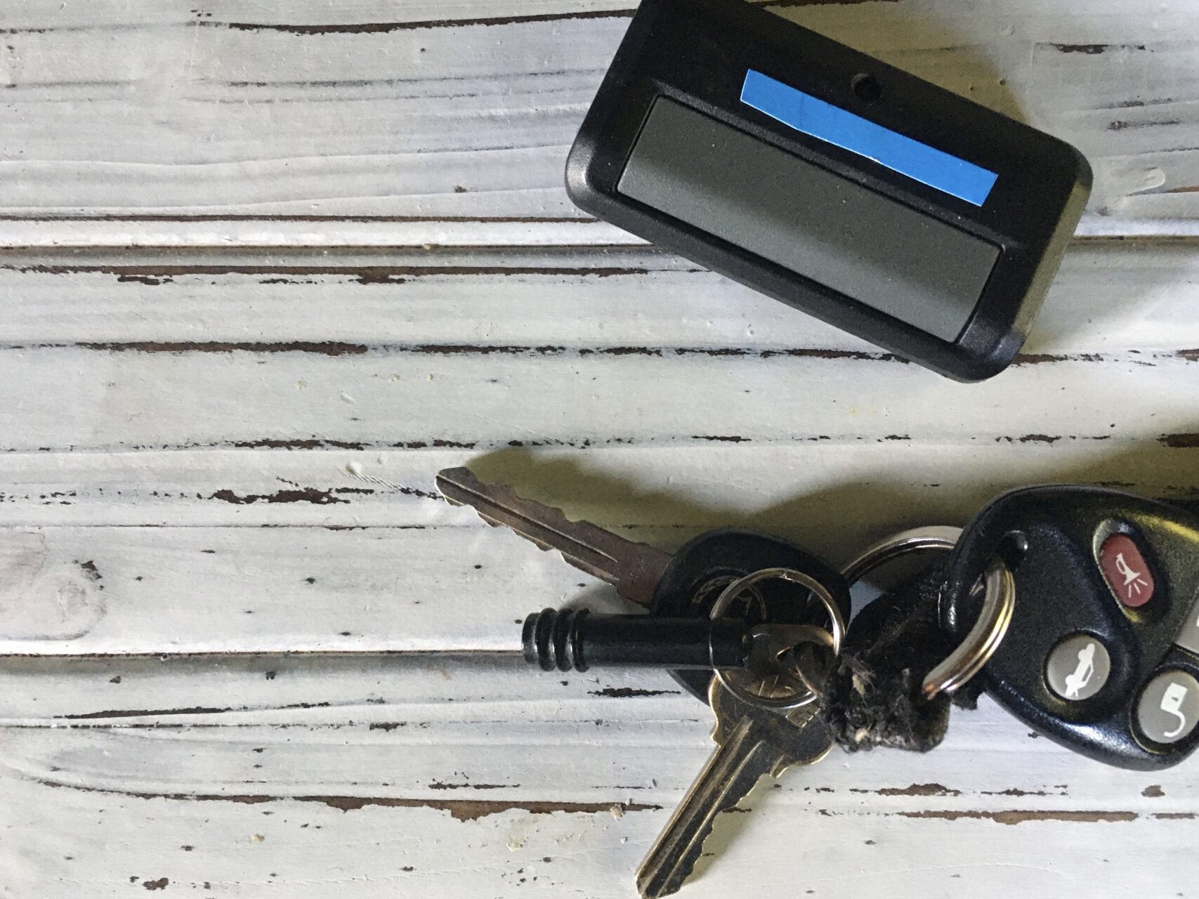 A remote garage door opener and a set of keys laying on a white table.